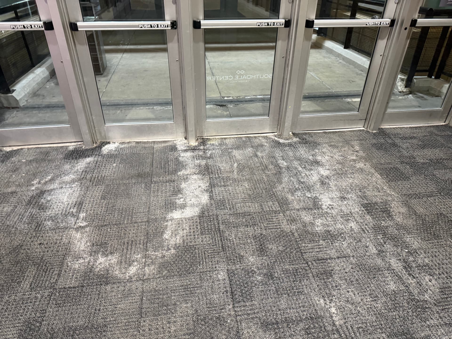 Heavy white salt residue tracked across commercial carpet tiles at a mall entrance